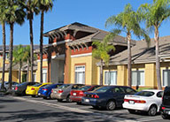 Photo of Irvine Inn main entrance in orange and red stucco, with palm trees and parking lot.